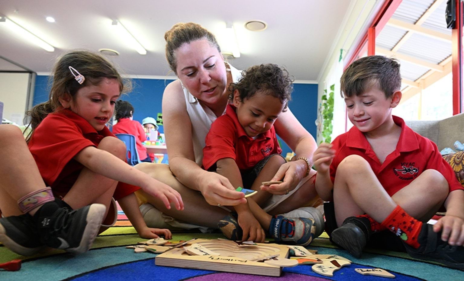 An educator and 3 students sitting cross legged on a mat solving a puzzle