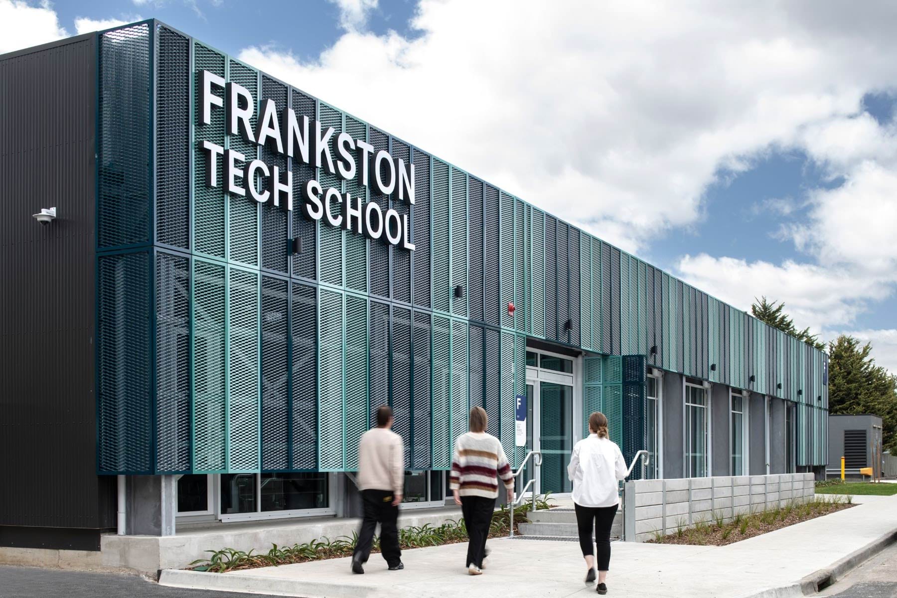 Exterior of Frankston Tech School building with large signage and three people walking toward the entrance.