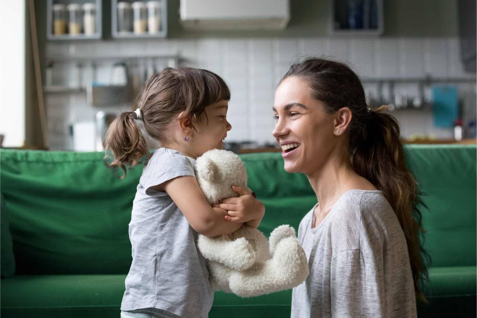 A woman and a child look at each other. Both are smiling. The child is holding a fluffy white teddy bear. 