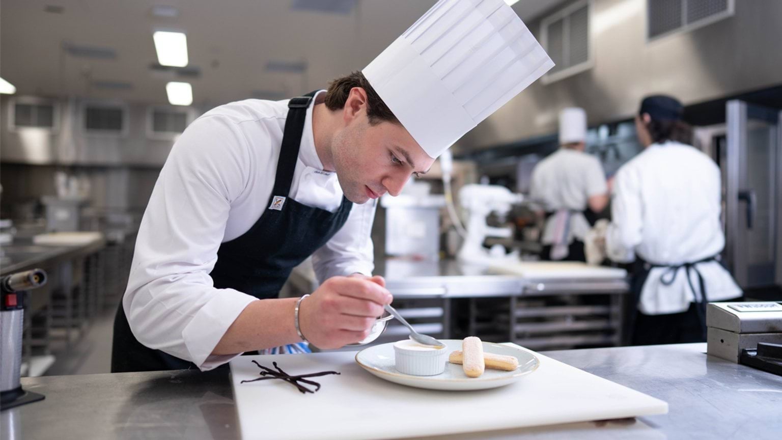 Student adding final touches to dish in a busy training kitchen