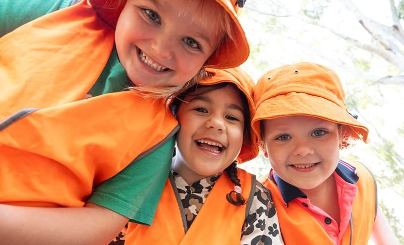 Three children wearing orange vests and hats, smiling