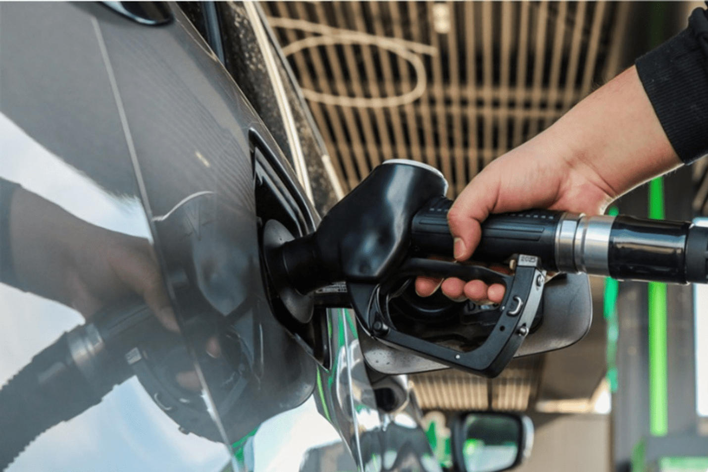 A hand on a fuel pump, pumping fuel into a grey car