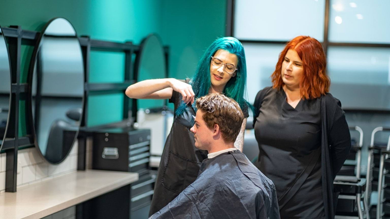 Student cutting a customer's hair whilst teacher is observing