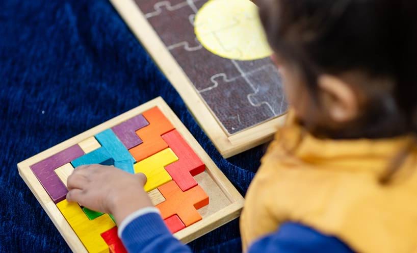 A child solving colorful wooden puzzle on a board