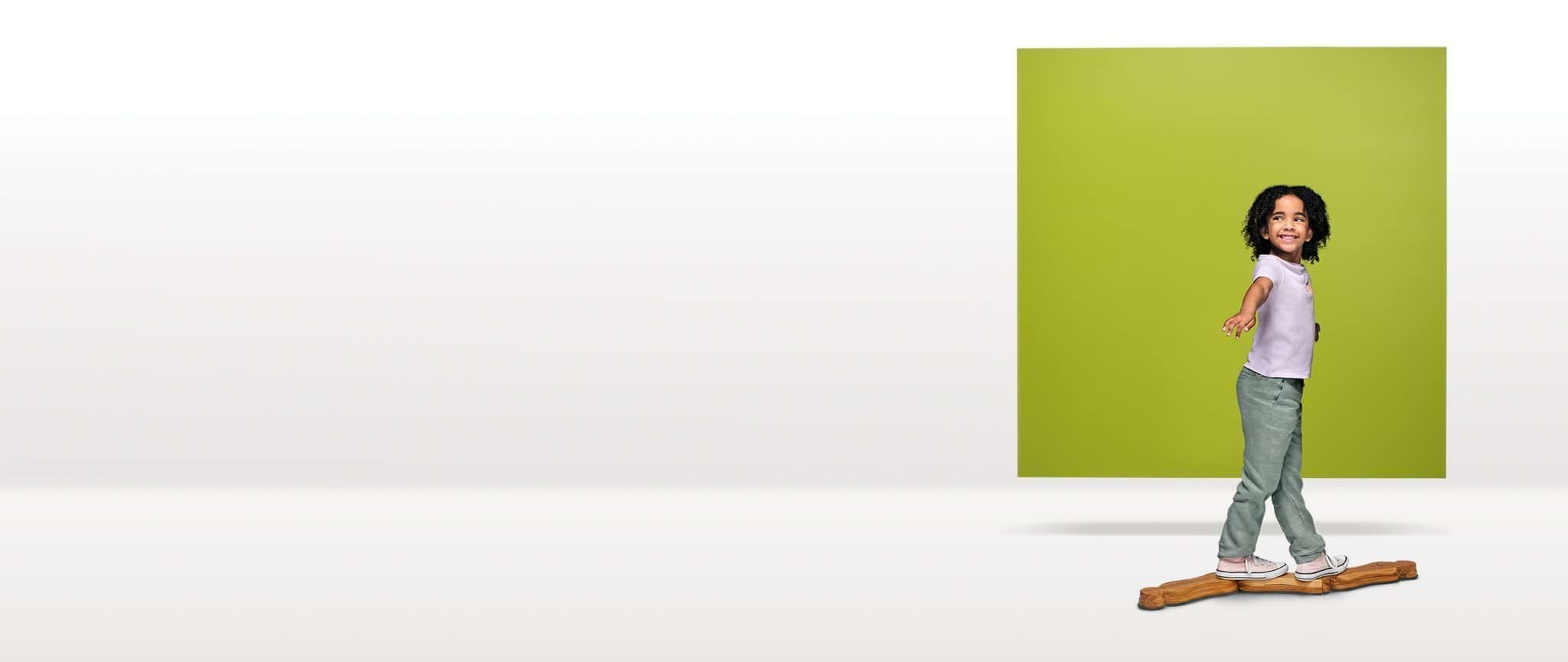 A 4-year-old child balances, walking on a log, in front of an olive-green square floating in a white space.