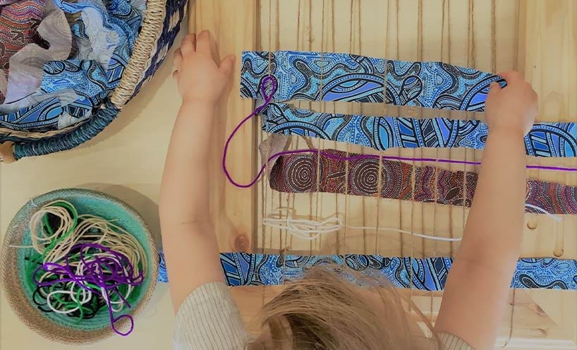 A child weaving with aboriginal print fabric strips