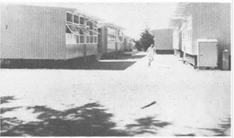 Black and white photo of a school with a number of portables with a large space in the middle, with a person walking through that space.