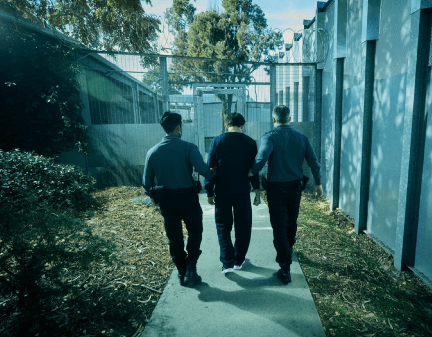 Young man being led into a secure facility by 2 officers.