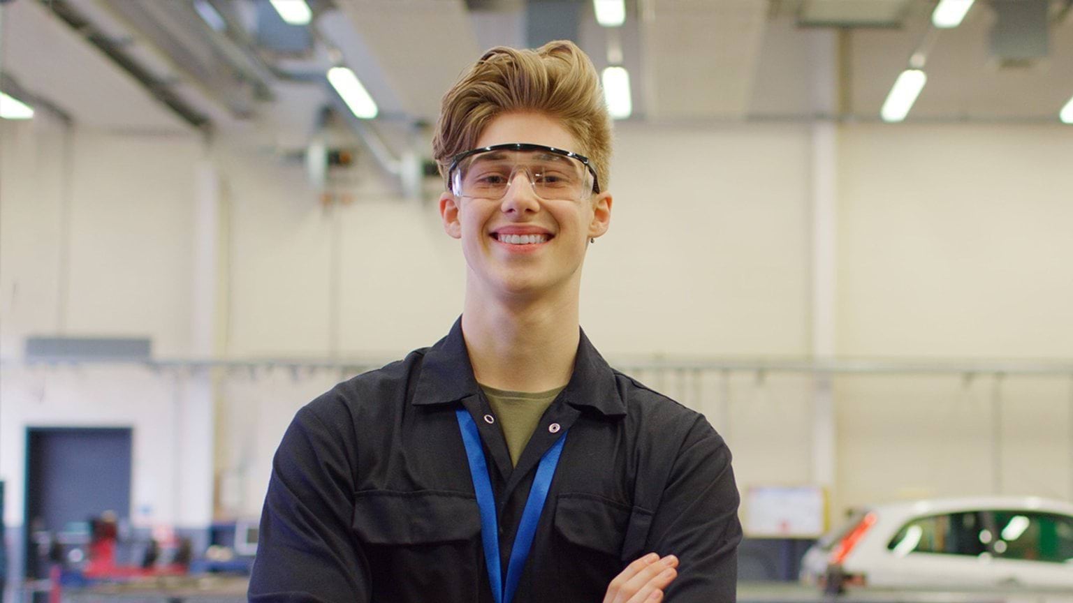 Student mechanic smiling into the camera in an automotive workshop