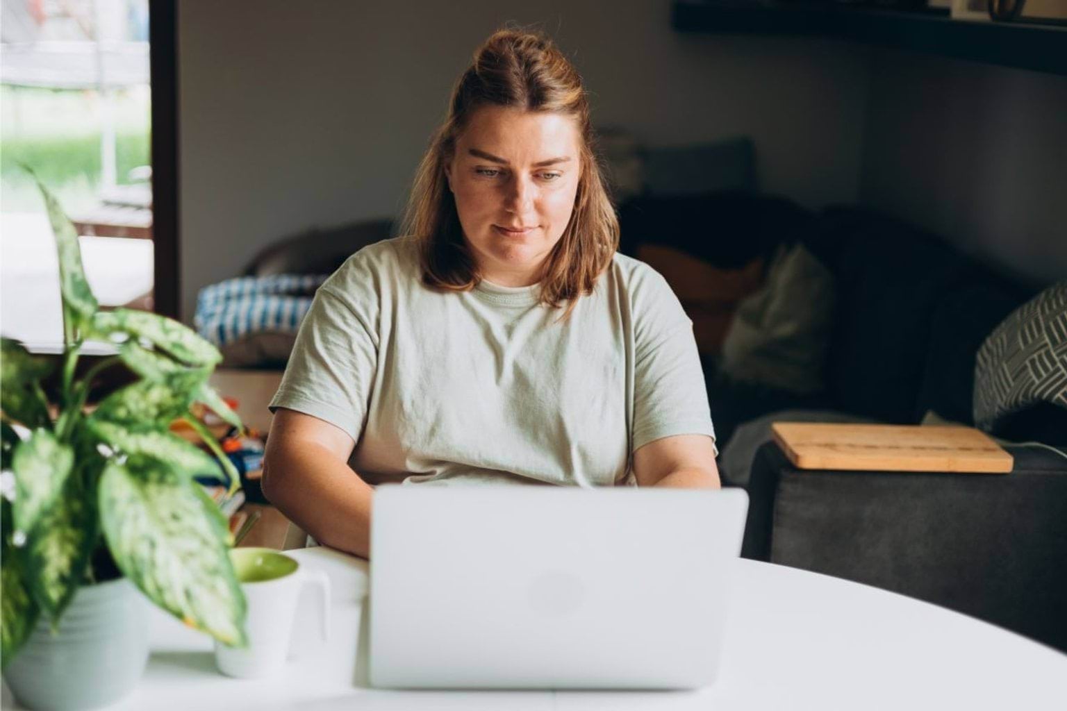 A woman sites indoors looking at a laptop. she is in a home.