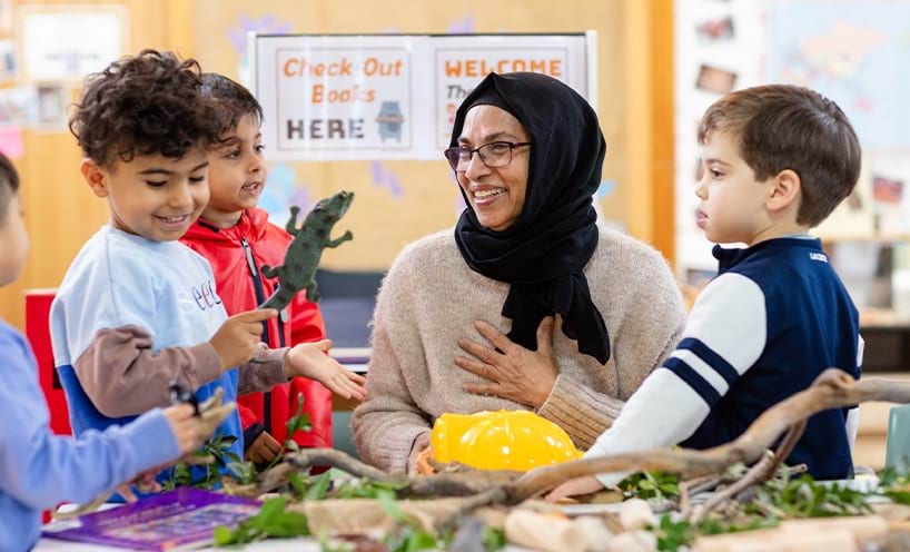 An educator smiling with children playing with resources around a table