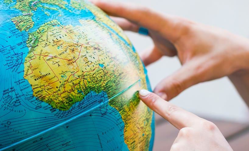 Finger pointing at a continent on the globe, the other hand holding the globe