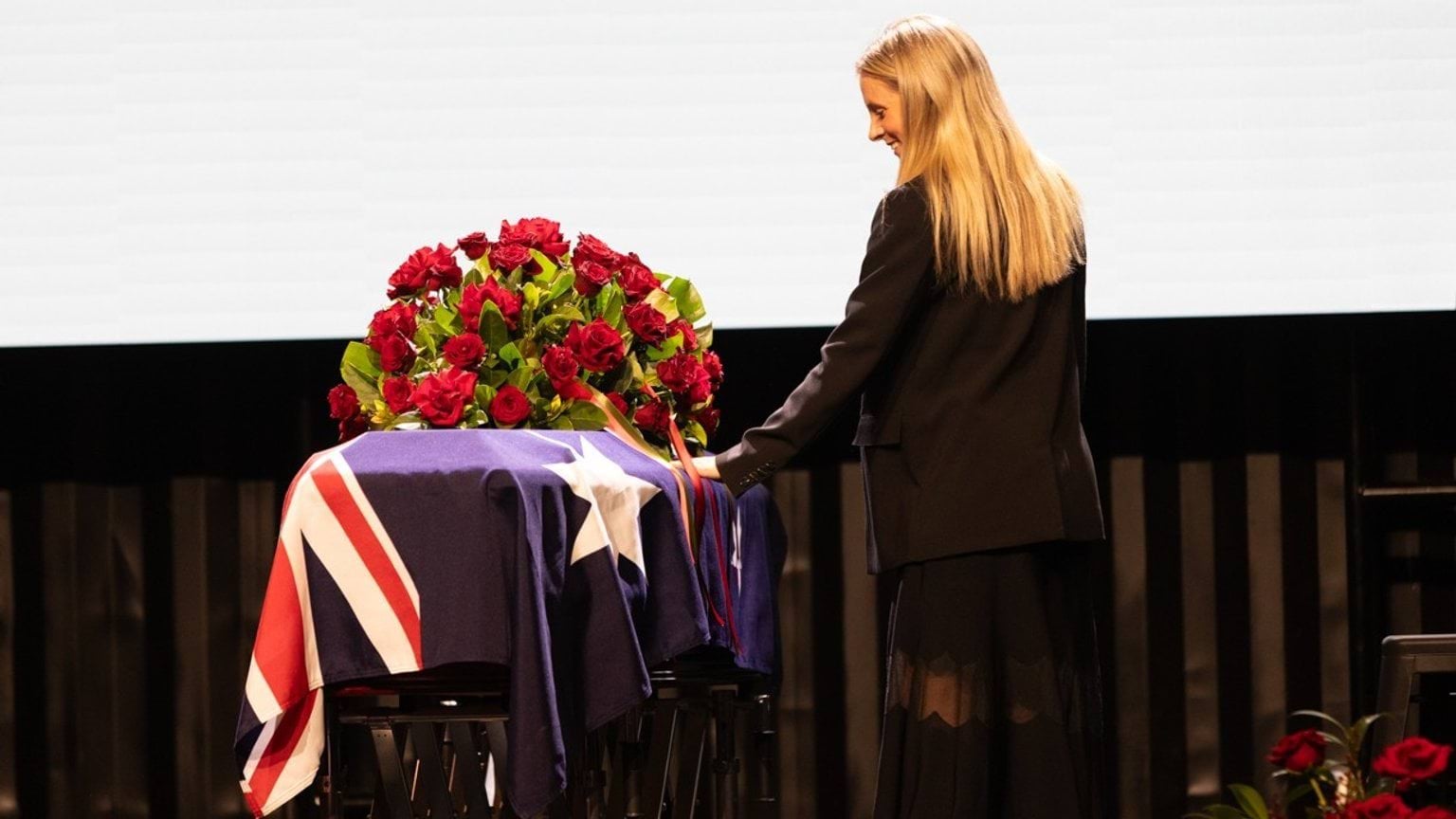 Ellie O'Connell, who performed the national anthem and an original song at the State Funeral Service of her godfather Derryn Hinch, touches his coffin while smiling