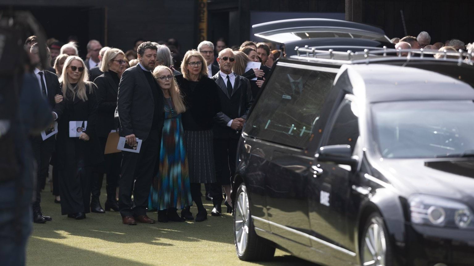 A group of mourners stand behind Derryn Hinch's hearse at the conclusion of his State Funeral Service