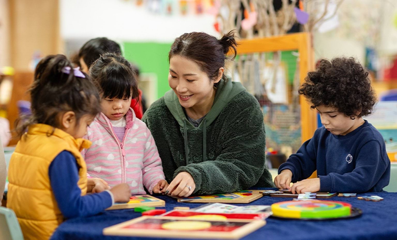 An educator assisting children solve board puzzles around a table