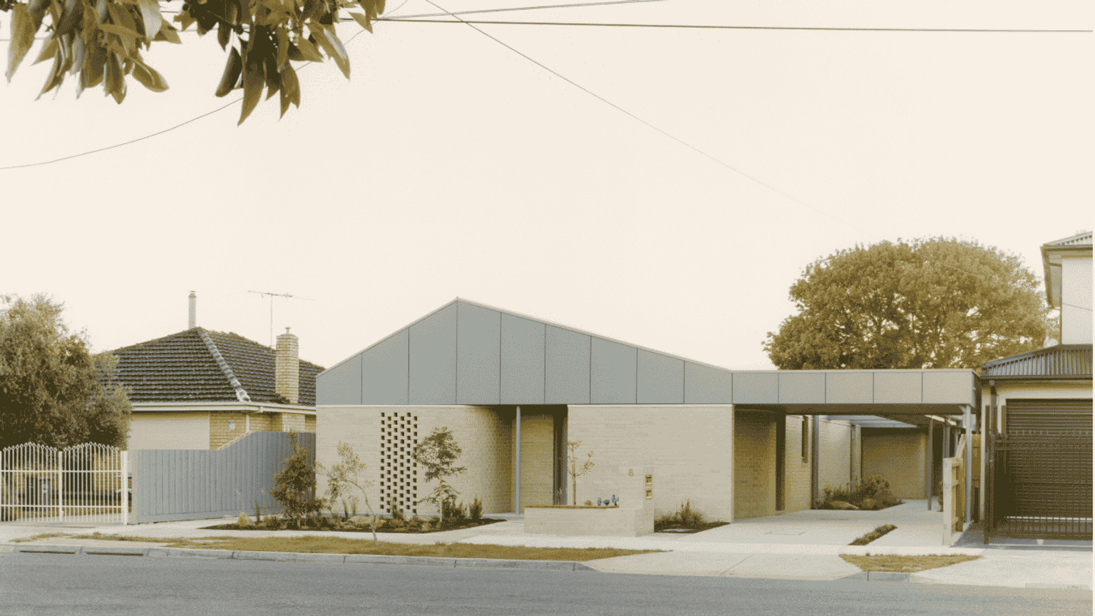 A modern house with a pointed roof and minimalist design, surrounded by greenery and set on a quiet street.