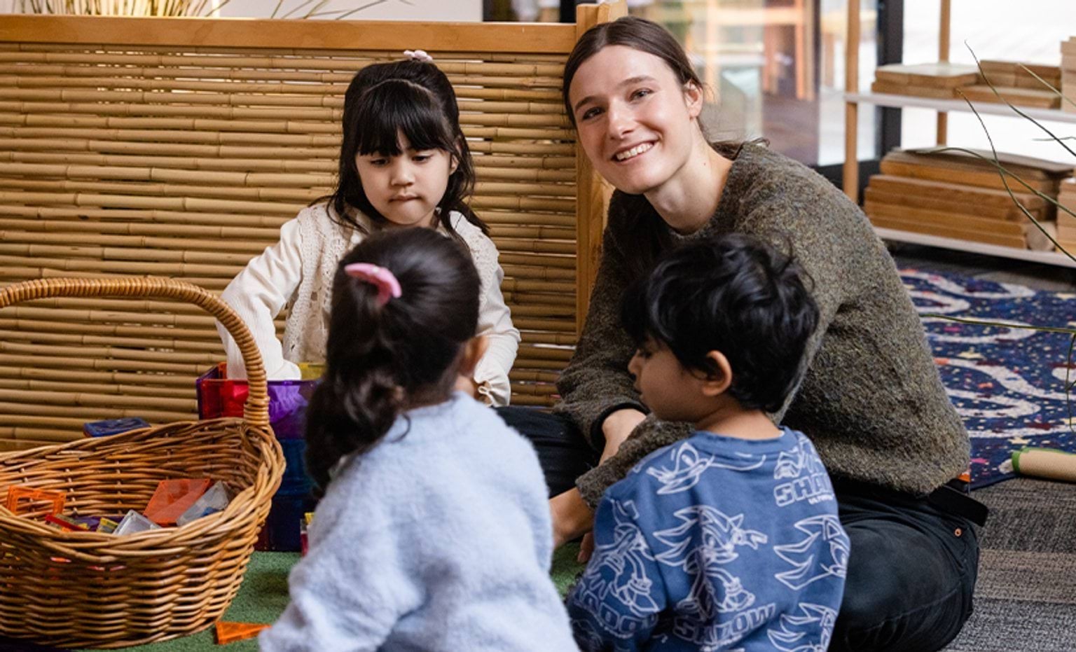 An early childhood educator smiling while assisting children play