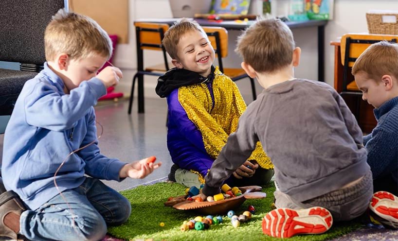 Children sitting on the floor in an early childhood setting, playing with wooden beads