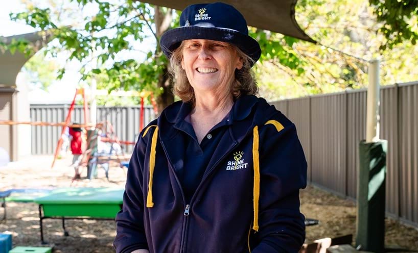 An early childhood educator smiling standing in outdoor play area