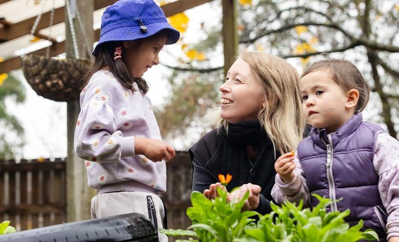 An educator interacting with one of the two children in outdoor play area