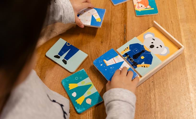 A child playing with a picture puzzle on the table, sat on a chair