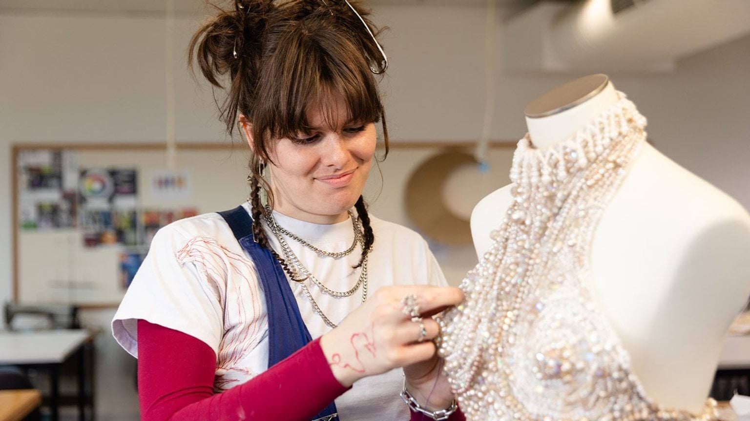 A person stitching a pearl dress on a mannequin
