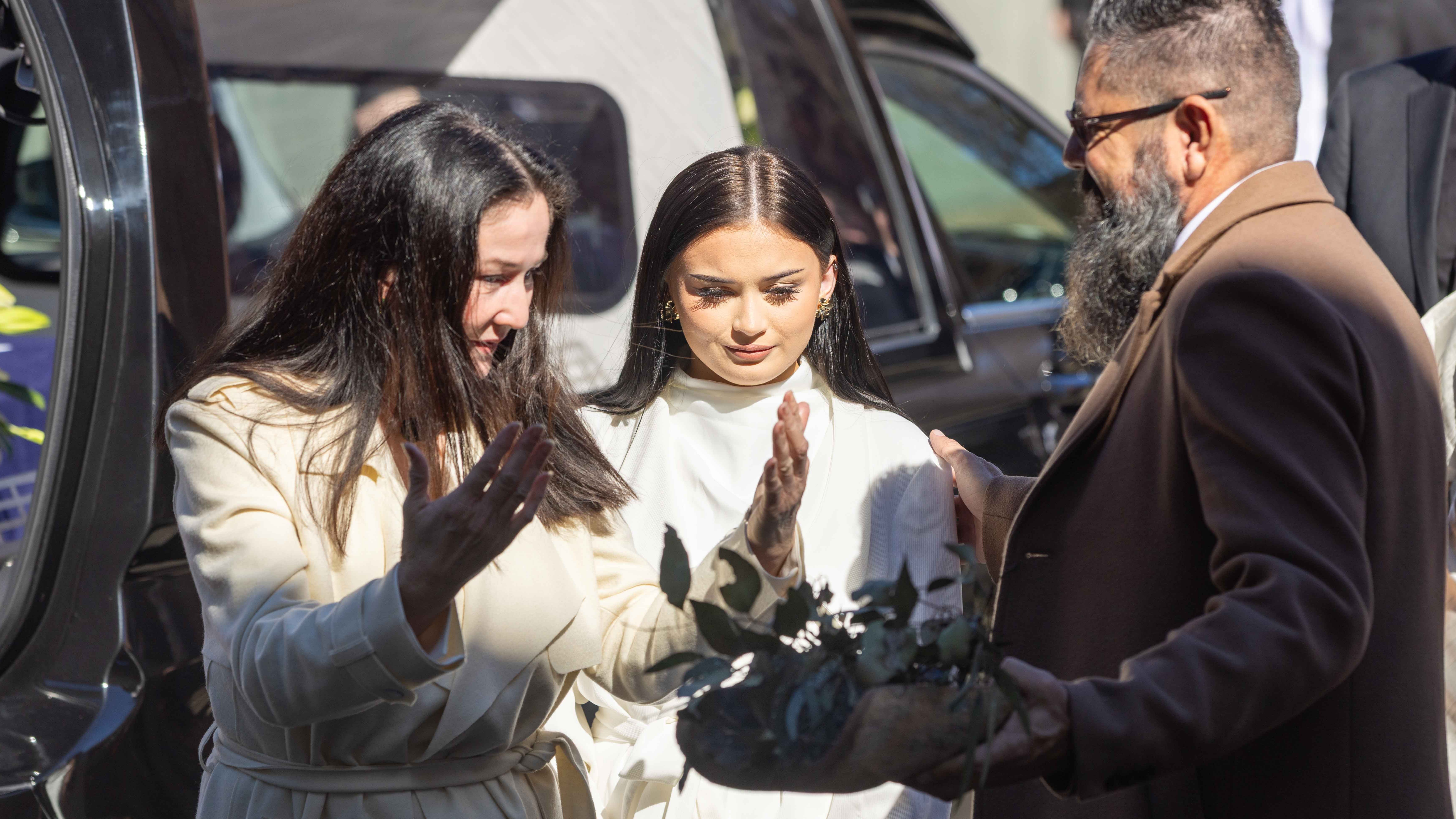 Russell's daughter and granddaughter take part in a Smoking Ceremony before the State Funeral Service. Russell's daughter Anita is moving her hands through the smoke, while standing in front of a Traditional Owner. Her daughter stands between the two.