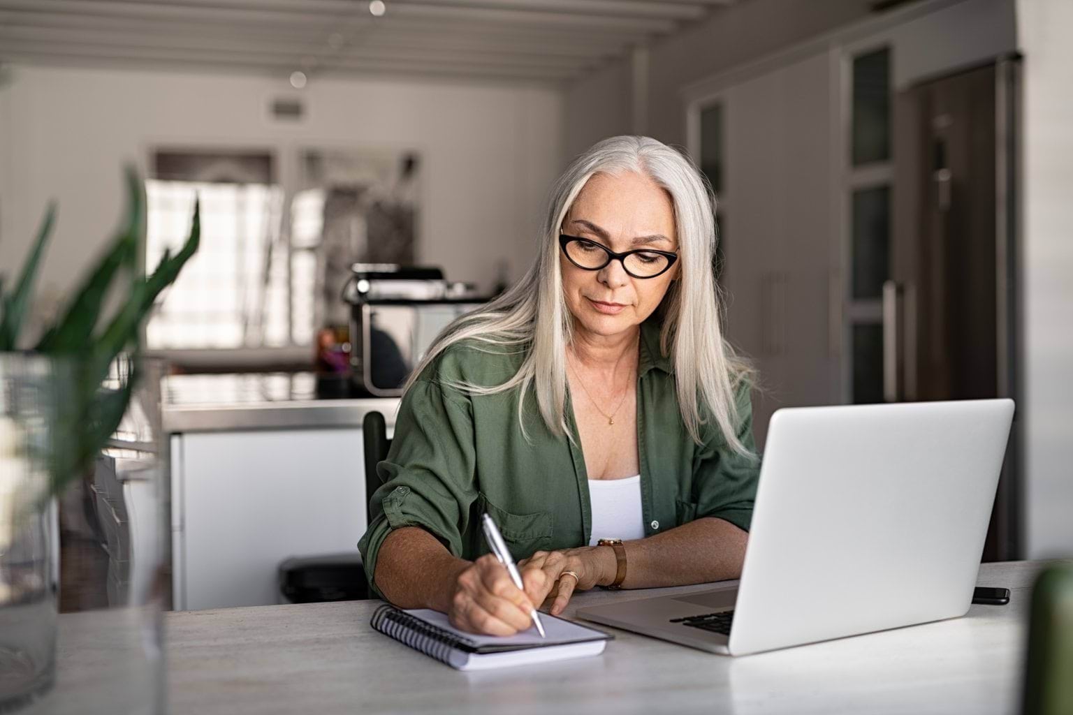 Women sits at computer writing in a notebook