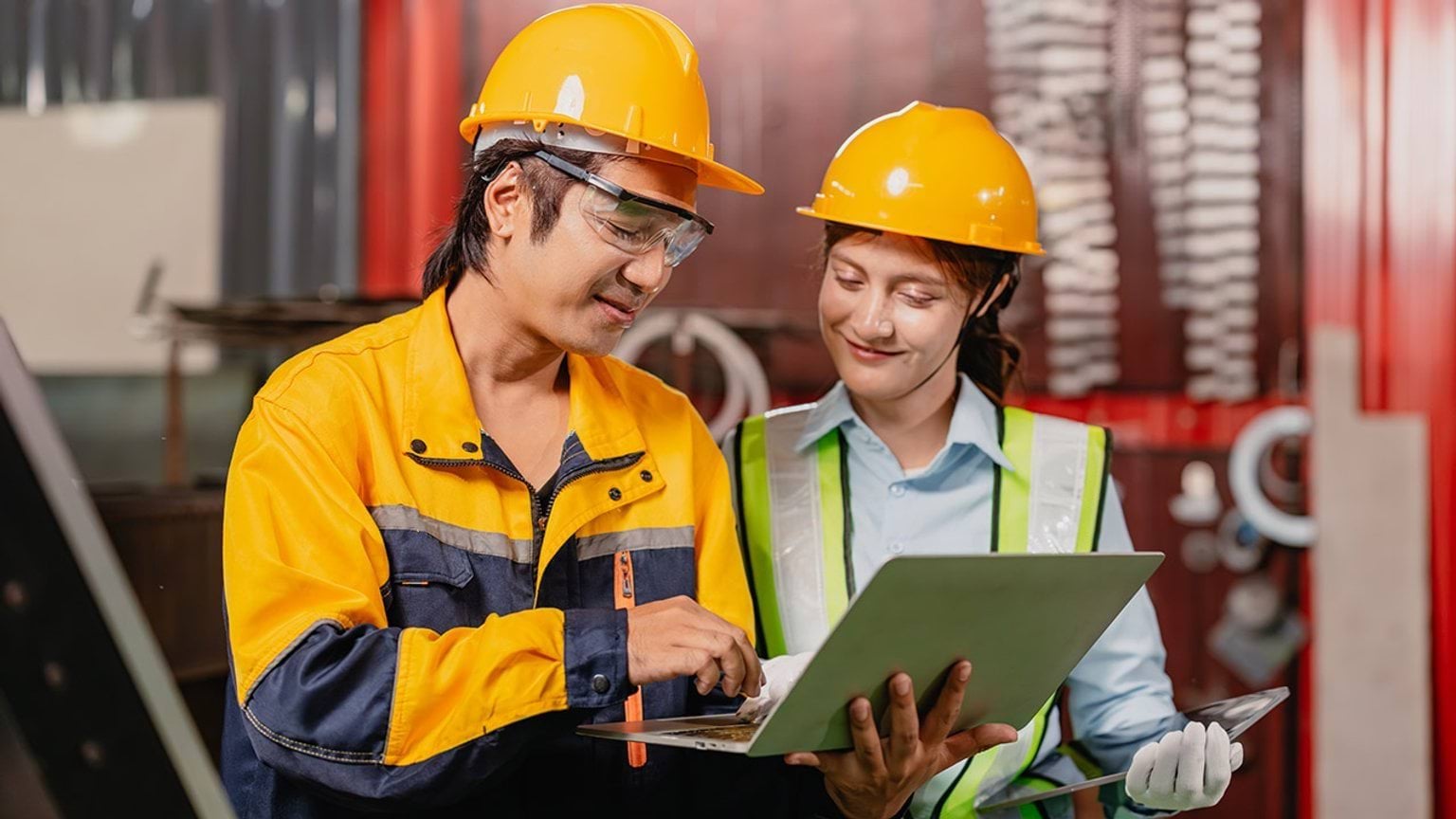 Two manufacturing workers wearing hard hats looking at paperwork