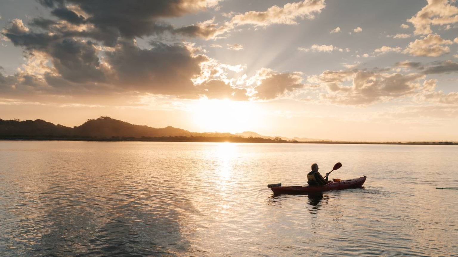 Person paddling a canoe on a lake during sunset