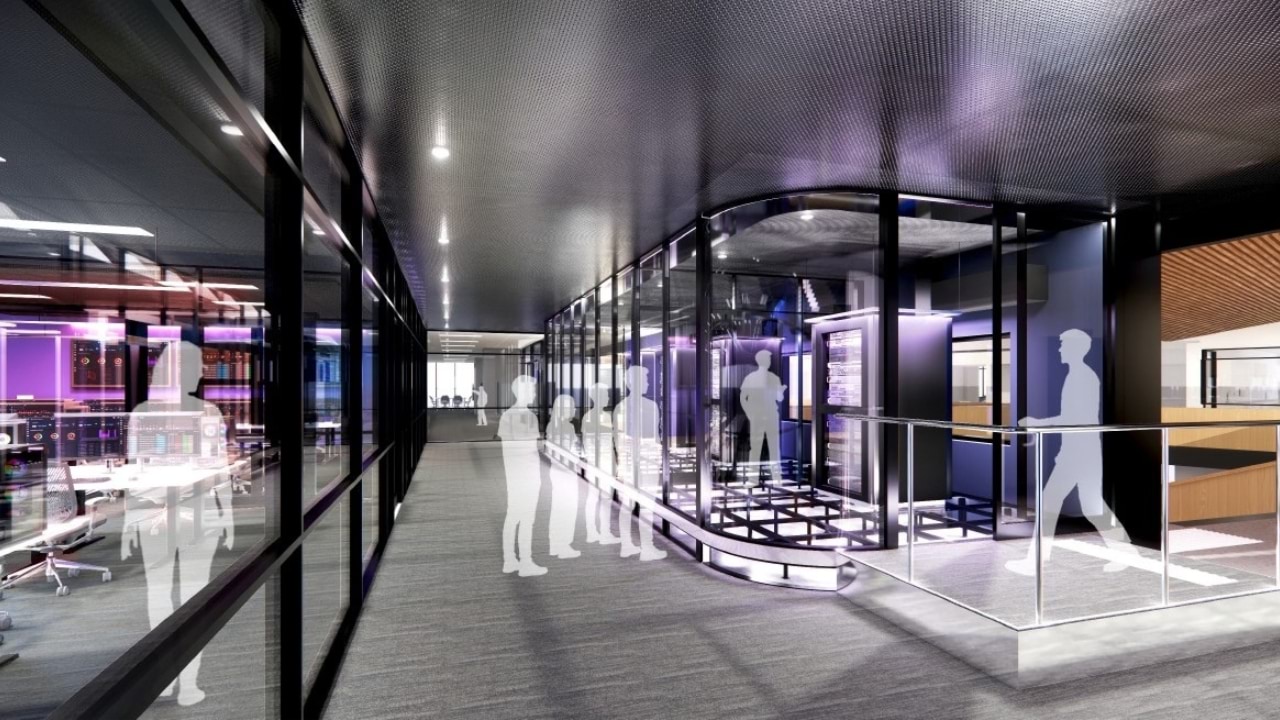 An artist's render of a high-tech interior space, likely a server room or tech hub, with sleek glass walls. The room features colorful lighting and digital displays on the left side, while silhouettes of people are walking and standing around a central glass-enclosed area.