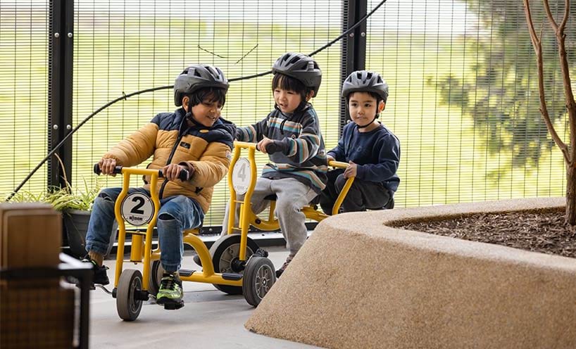 Three children riding tricycles around a play scape.