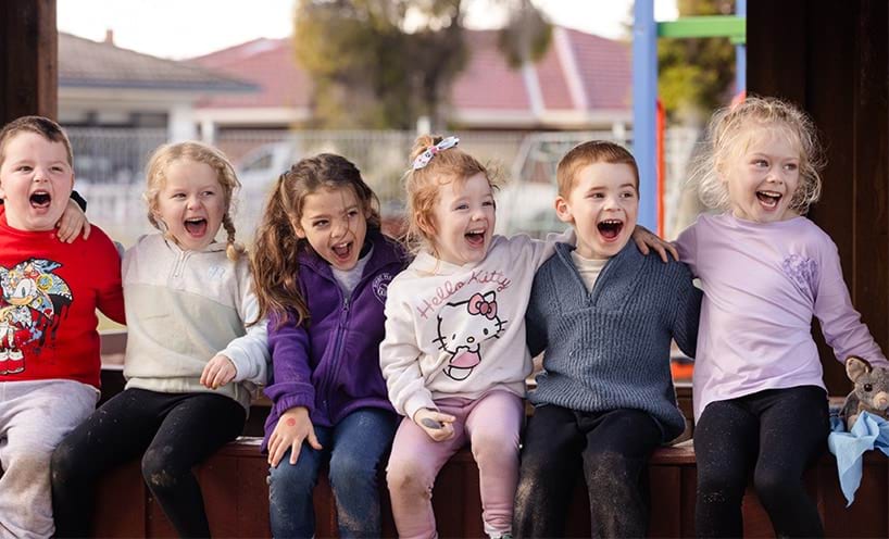 Six children sitting arm-in-arm laughing.