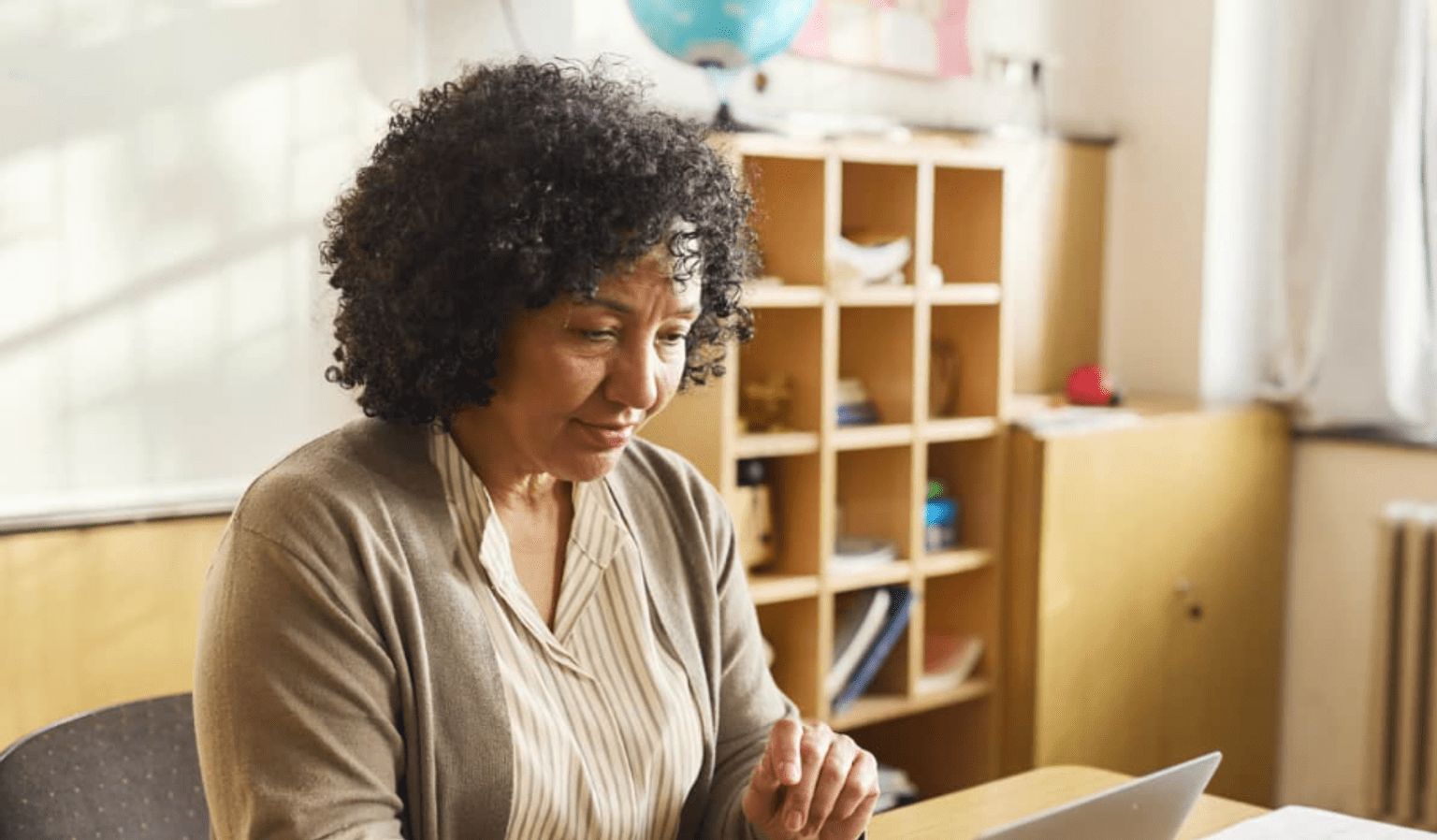 A woman sits at a desk in an educational setting at a lap top.