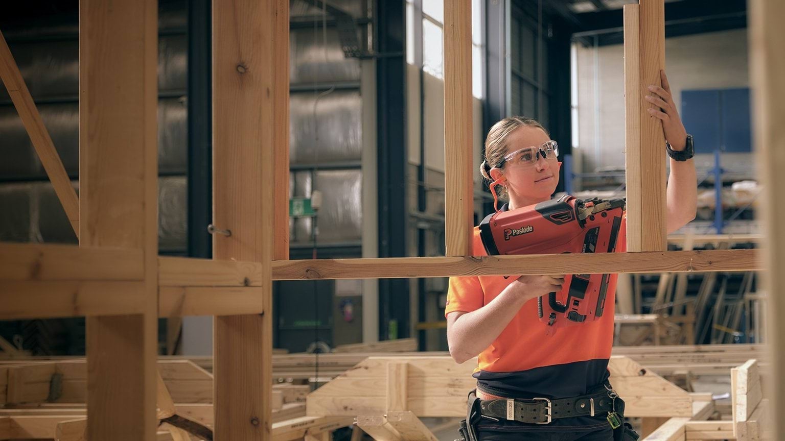A person in safety glasses uses a nail gun on a wooden frame.