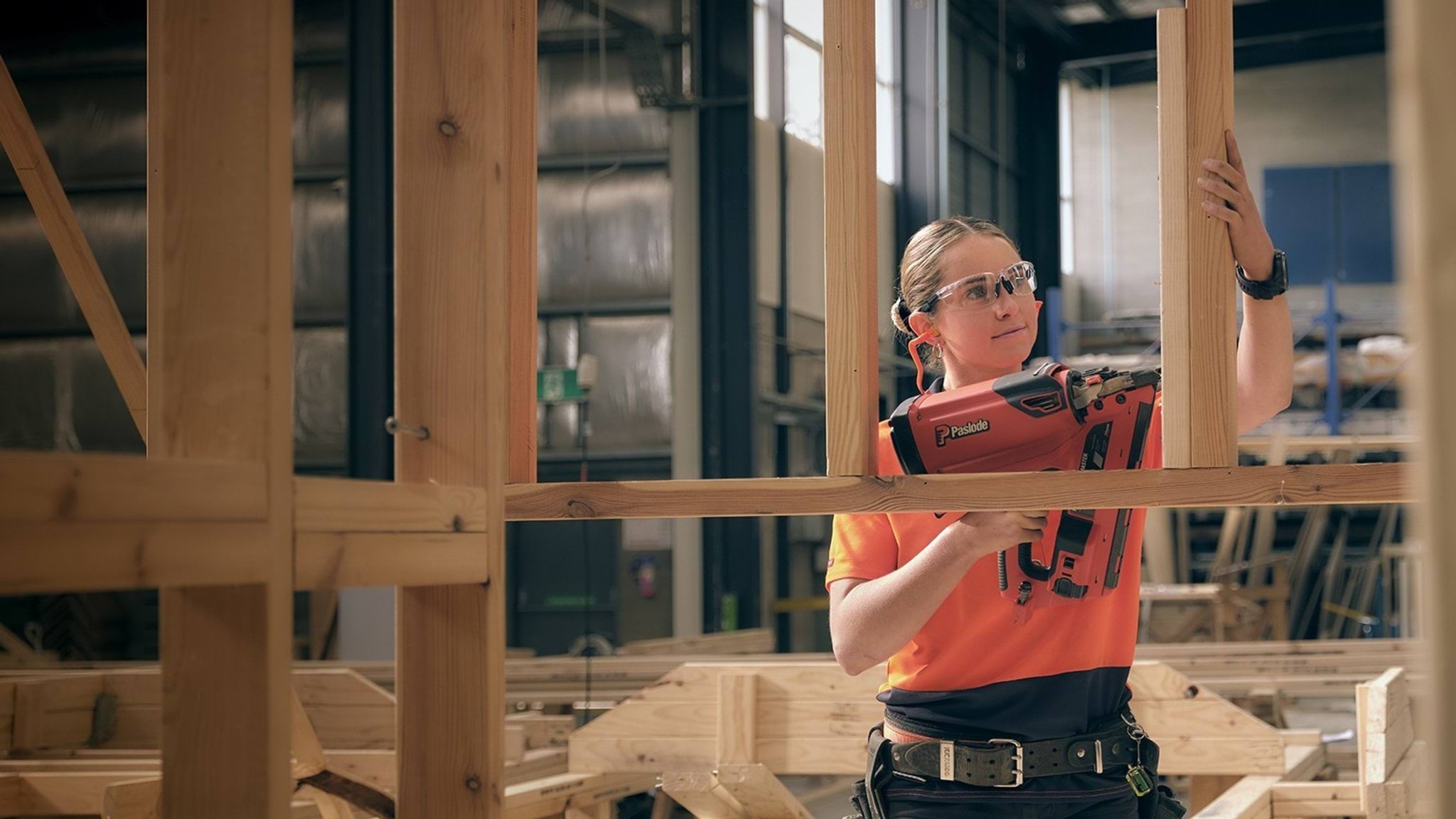 A person in safety glasses uses a nail gun on a wooden frame.