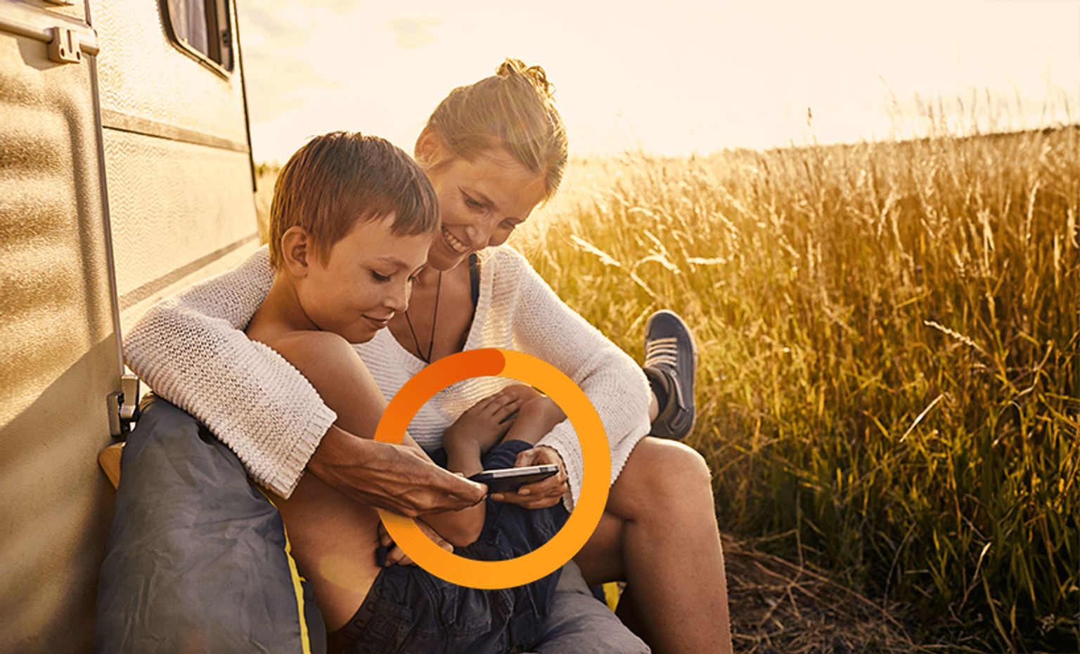 Mother and son in field on phone A mother and son are hugging, leaning against a white truck in a field of golden light, smiling and looking at phone